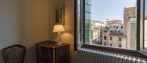 A room with a view of a cityscape through a window, a radiator, a wooden cabinet, and a chair.