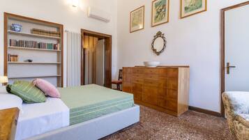 Un dormitorio con cama, cómoda de madera, estantería y radiador.