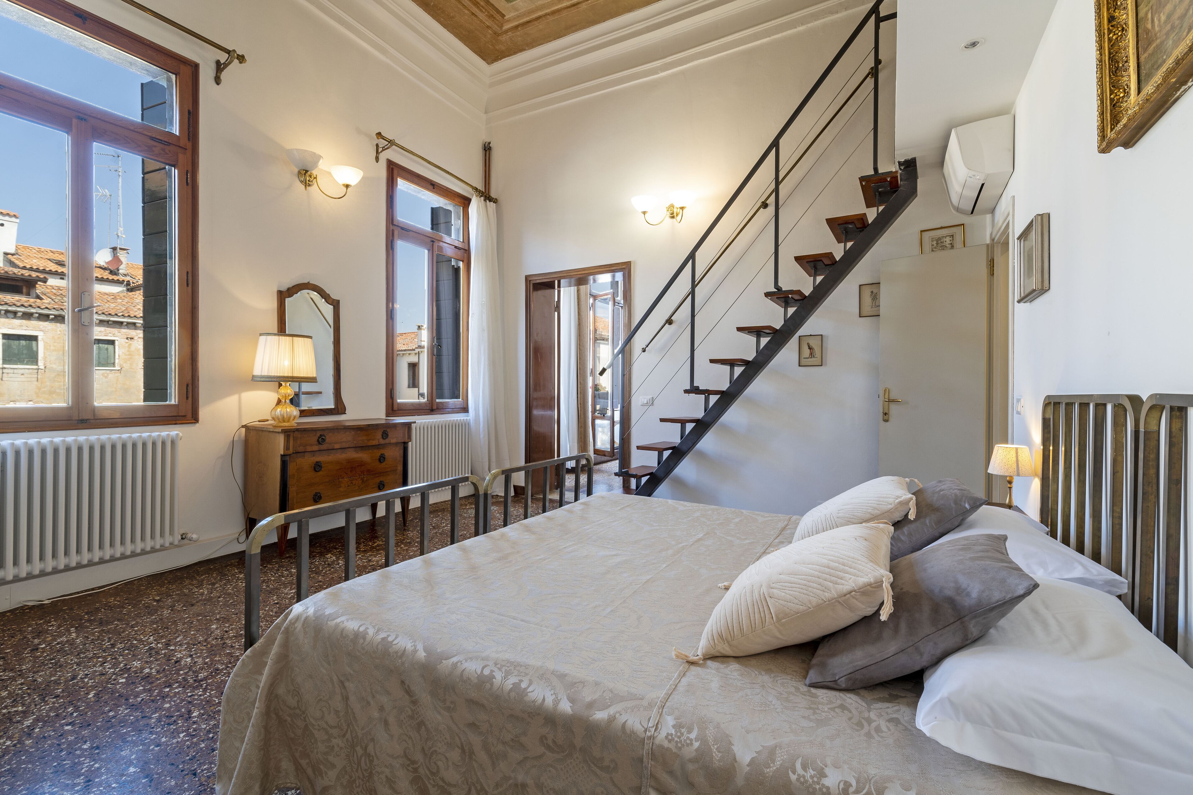 A bedroom with a bed, a dresser, a mirror, a window, and a staircase.