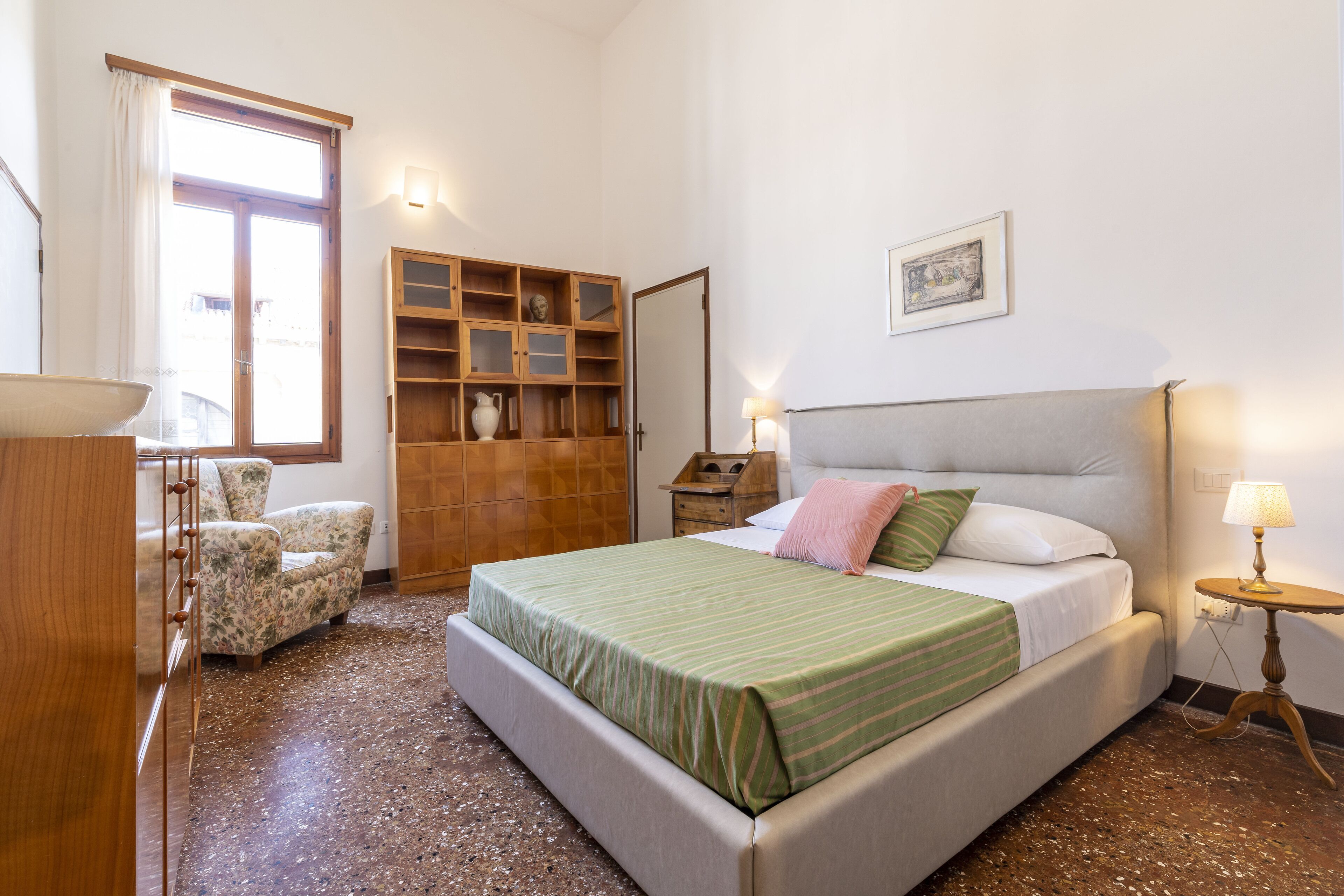 A bedroom with a bed, a chair, a wooden cabinet, and a small table with a lamp.