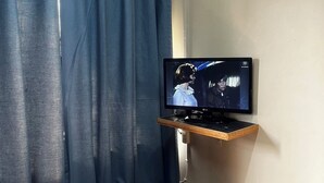 Een televisie aan de muur, een houten bank en blauwe gordijnen.
