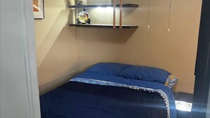 Een slaapkamer met een bed, een plafondventilator en planken met spullen.