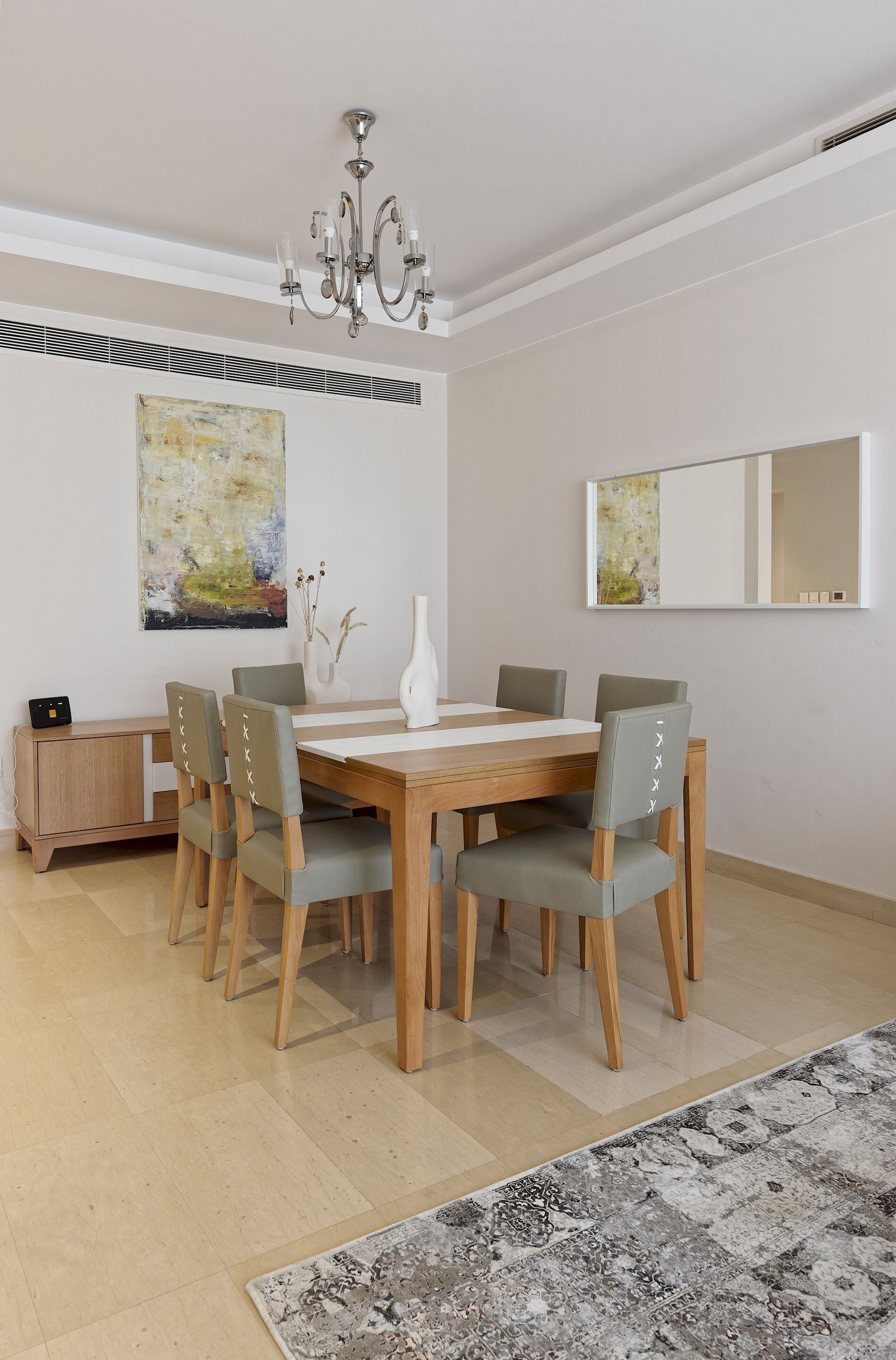 A dining area with a wooden table and six chairs, a chandelier, and two abstract paintings on the walls.