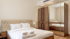 Een net opgemaakt bed met witte lakens en opgevouwen handdoeken, een houten hoofdbord en een groot spiegelkast met een houten afwerking.