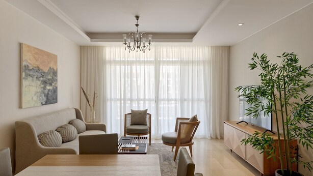 Een moderne woonkamer met een eettafel, banken, stoelen, een grote potplant en een kroonluchter.
