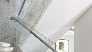 A marble staircase with glass railings leading to a living area with a red sofa and a framed artwork.