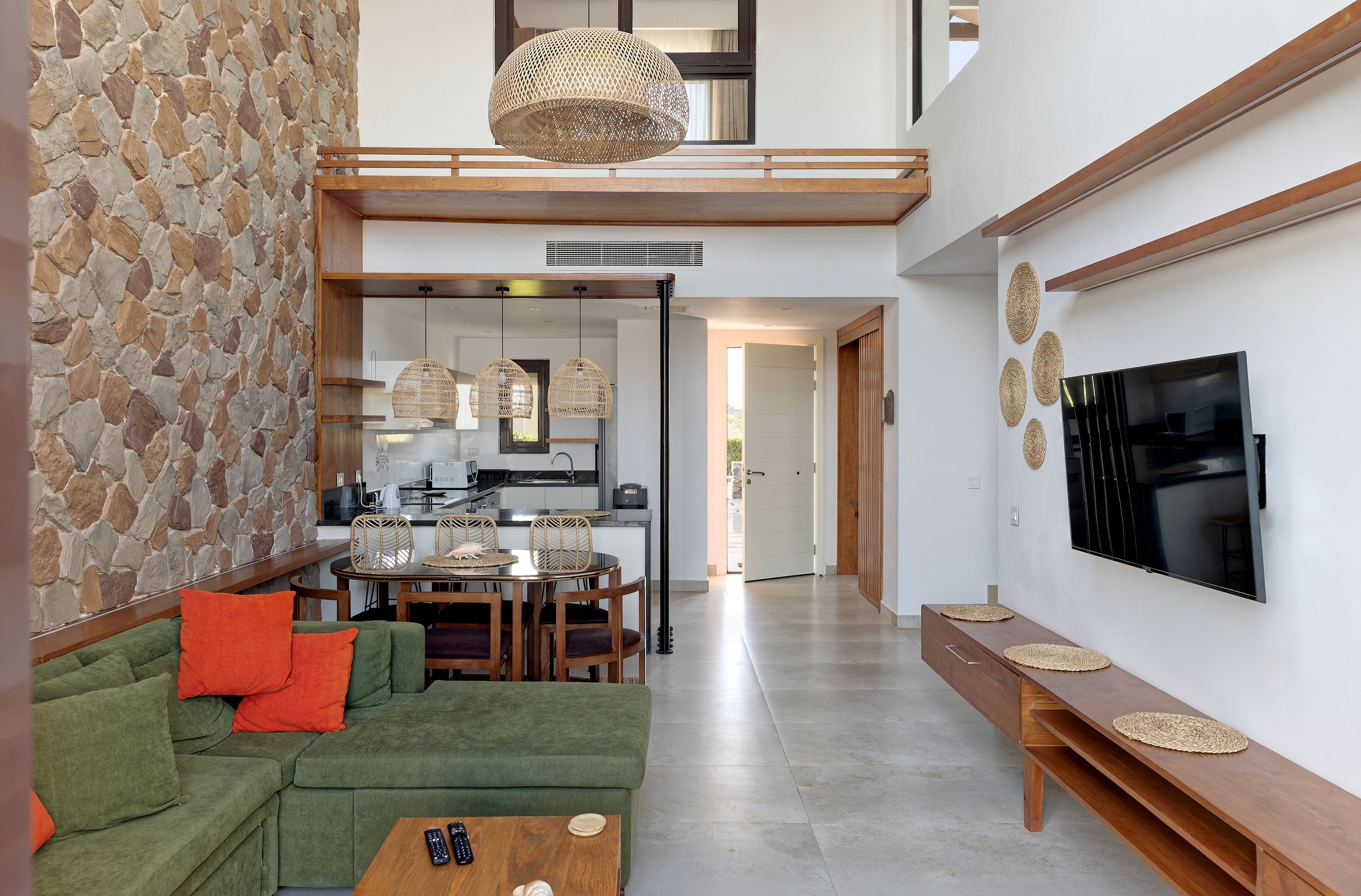 Un salon moderne avec un mur en pierre, un canapé vert et un coin repas avec des chaises en osier.