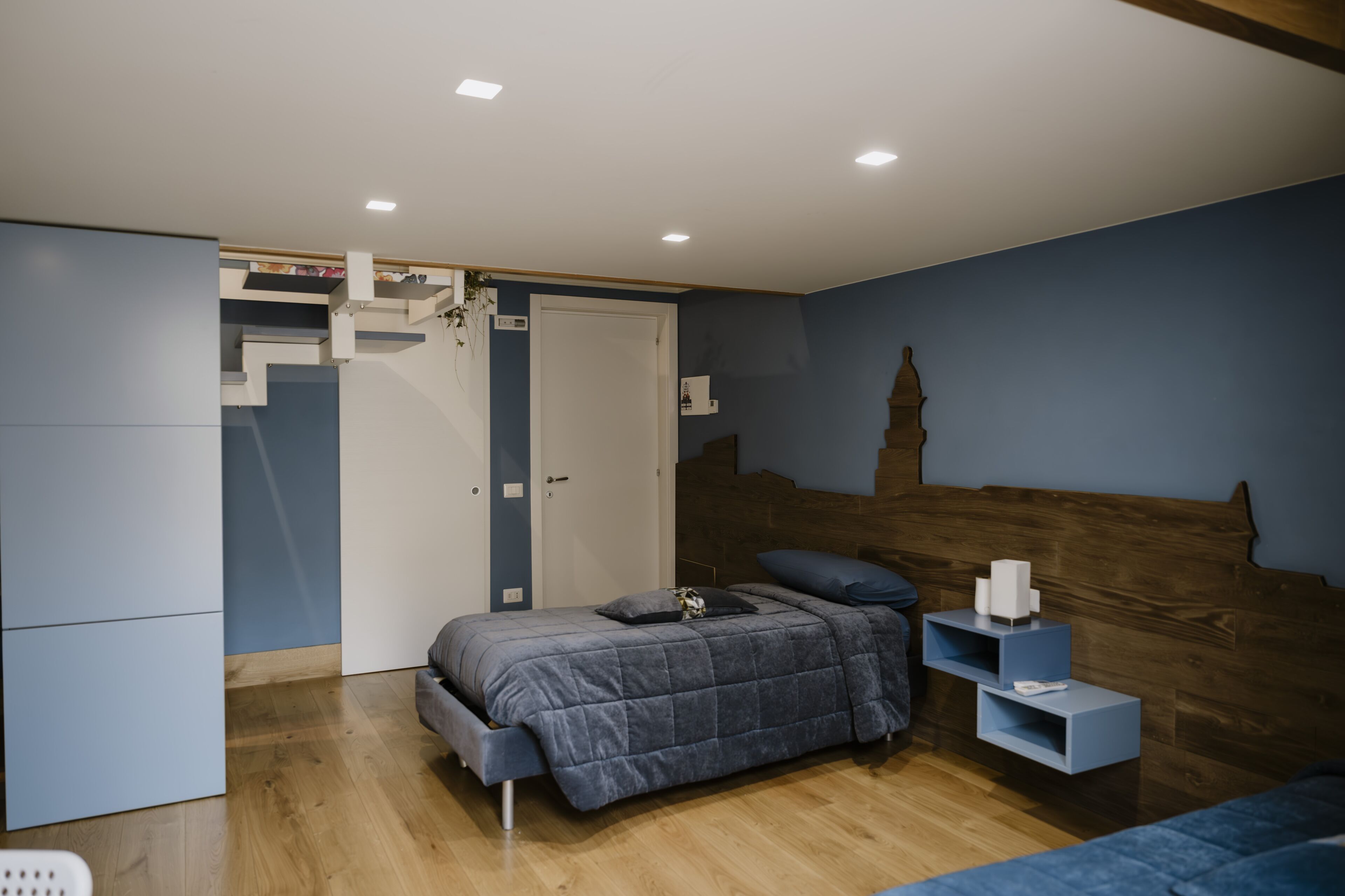 Un dormitorio con cama, armario, mesita de noche y estante en la pared.