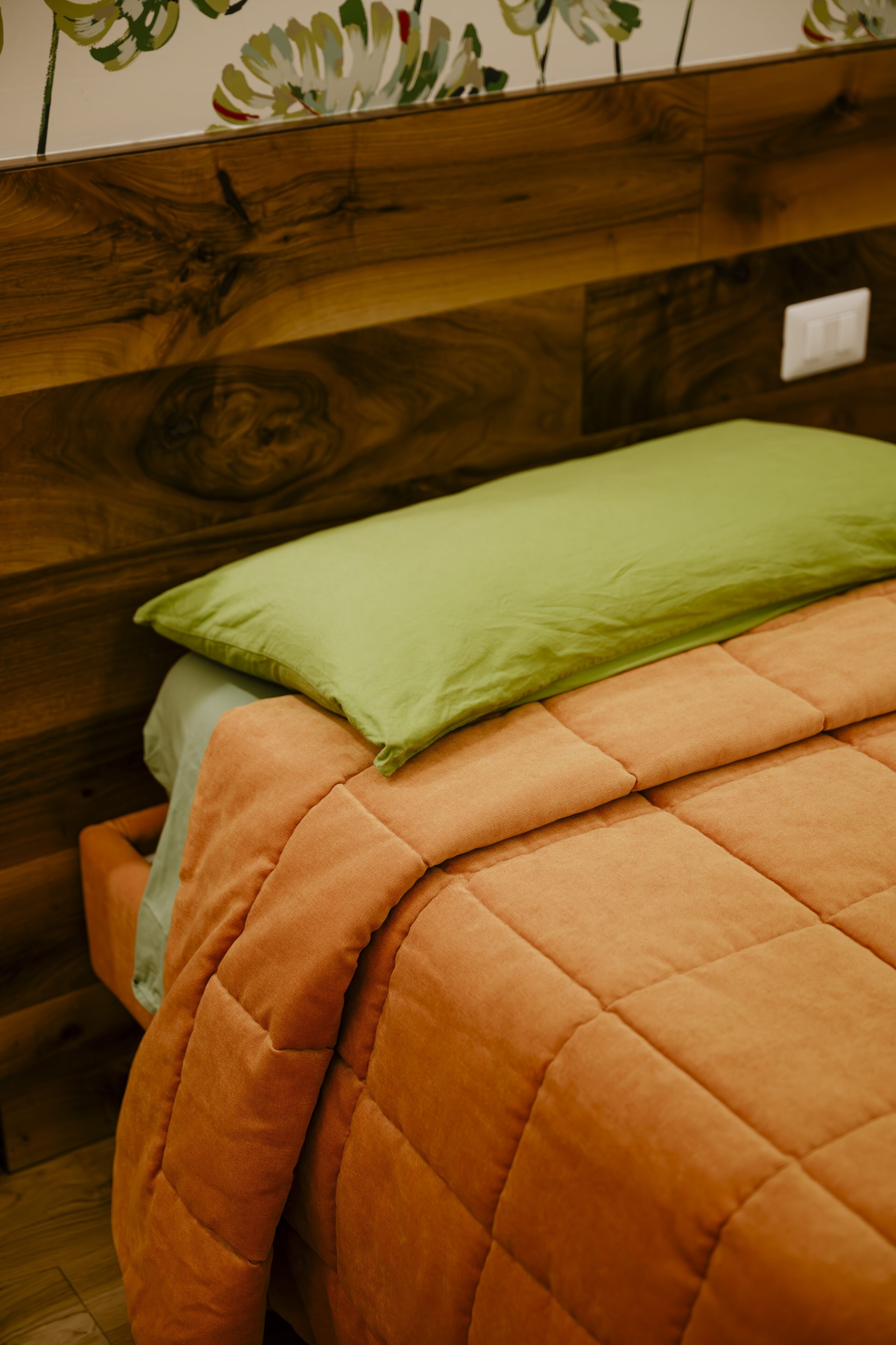 Una cama con un edredón naranja y una almohada verde.