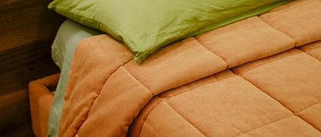 Una cama con un edredón naranja y una almohada verde.
