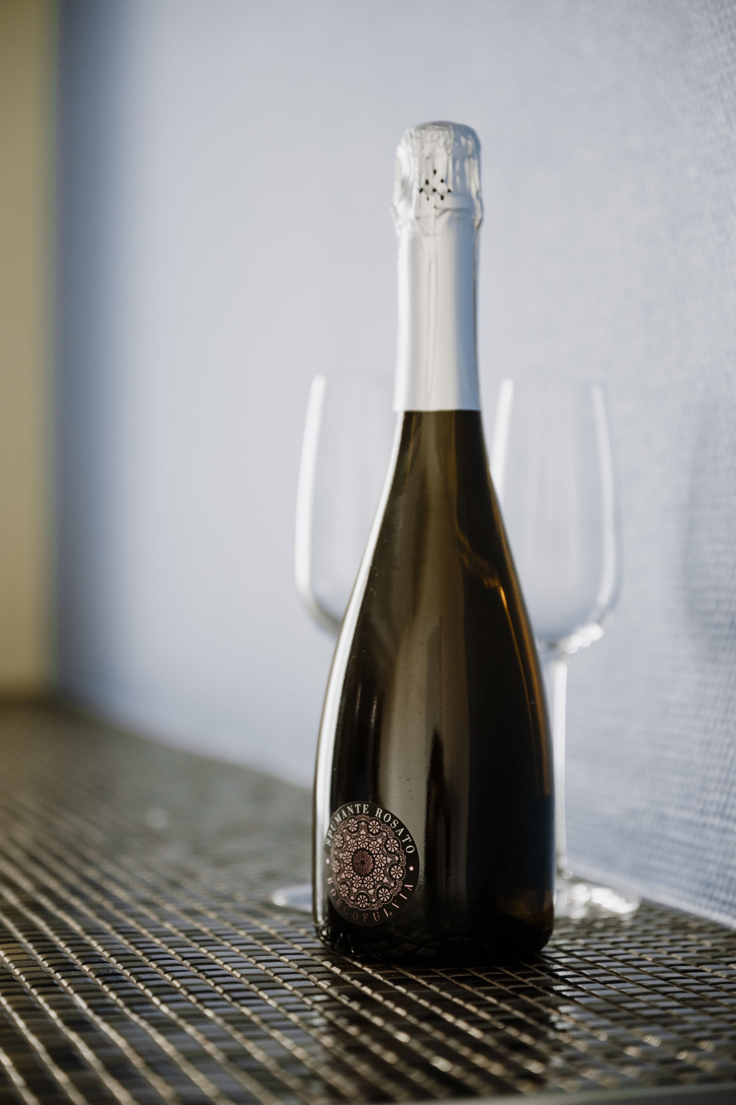 Una botella de vino sobre una mesa de metal con dos copas de vino vacías a su lado.