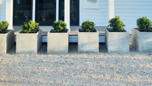 A white building with a number '9' sign, a covered entrance, and six planters with shrubs. - 9 Academy (Salisbury)