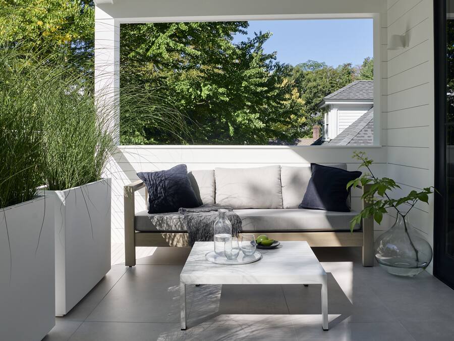 Un espace de détente extérieur moderne, avec un canapé blanc, une table basse en marbre et un vase en verre contenant une plante.