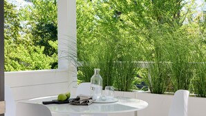 A modern outdoor dining area with a round table and white chairs, surrounded by lush greenery and a white railing. - 9 Academy (Salisbury)