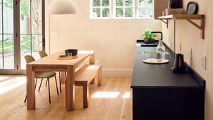 A modern kitchen with a wooden dining table, chairs, a pendant light, and a black countertop with a coffee maker and a plant. - 9 Academy (Salisbury)