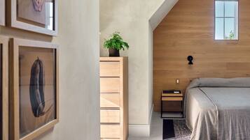 A modern bedroom with a wooden ceiling, a bed, a nightstand, a dresser, and framed artwork on the wall.