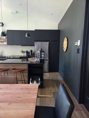 A modern kitchen with a central island, black cabinets, and a stainless steel refrigerator.
