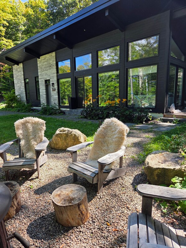 A modern building with large windows and a gravel patio with wooden chairs and tables.