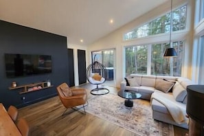 En moderne stue med en mørk væg, et stort vindue, en sofa, et sofabord og en hængestol.