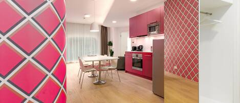 A modern kitchen with pink cabinets, a microwave, and a dining area with a white table and chairs.