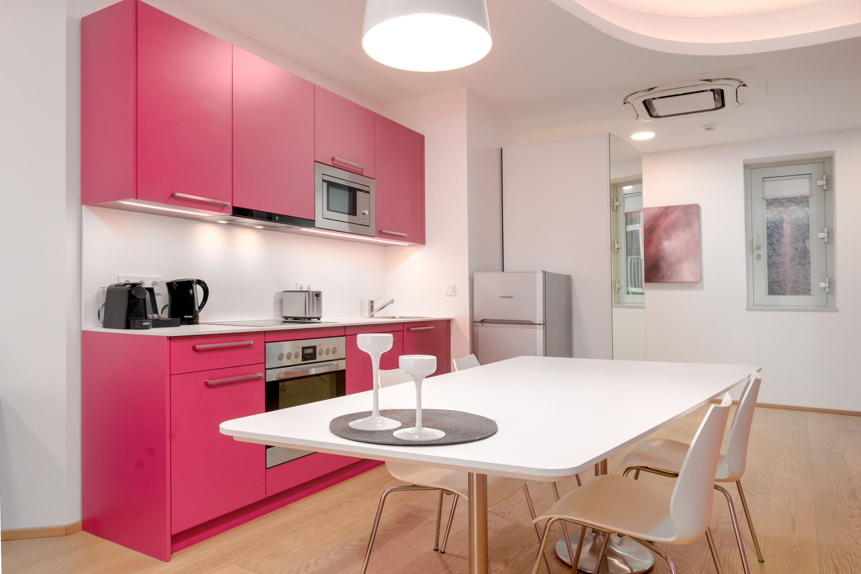 Et moderne køkken med pink skabe, et hvidt spisebord og et minimalistisk design.