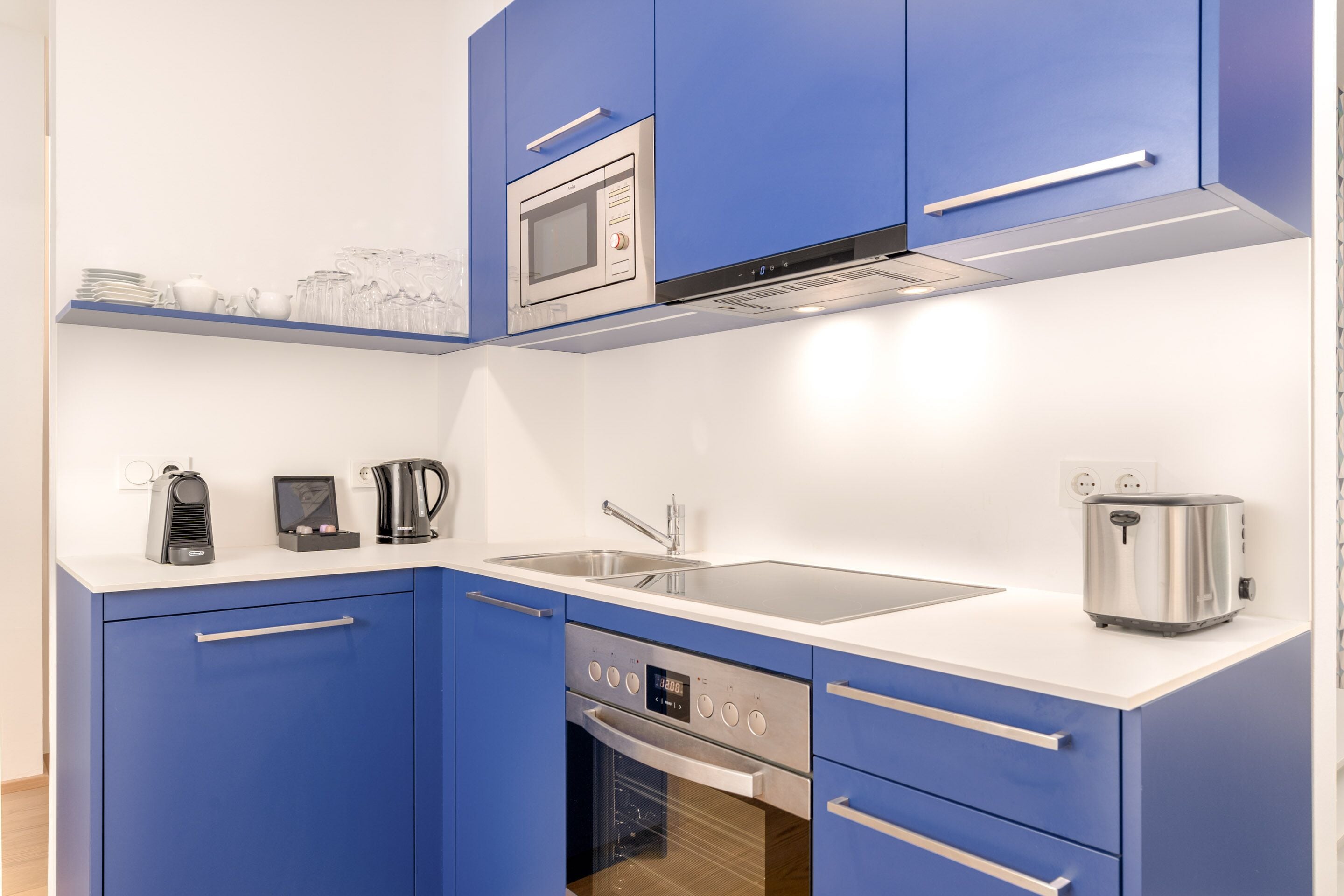 Una cocina moderna con armarios azules, microondas integrado, cafetera, tostadora y lavavajillas.