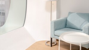 Une pièce moderne avec une fenêtre incurvée, un canapé bleu clair, une table blanche et un lampadaire.