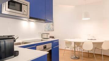 A modern kitchen with blue cabinets, a microwave, a toaster, and a dining area with a white table and chairs.