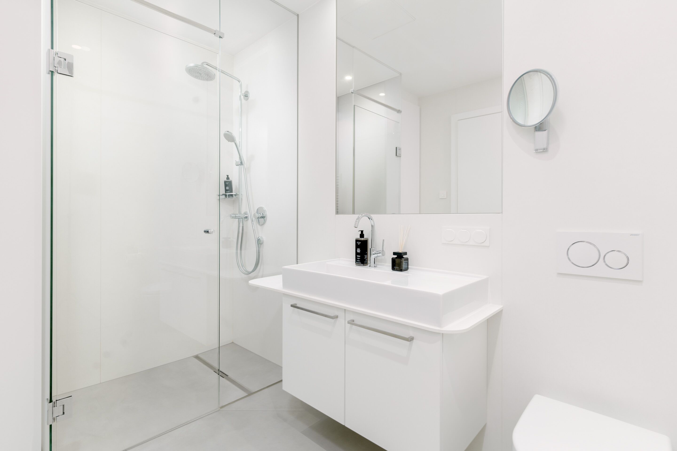 A modern bathroom with a glass shower enclosure, a white sink with a mirror, and a toilet.
