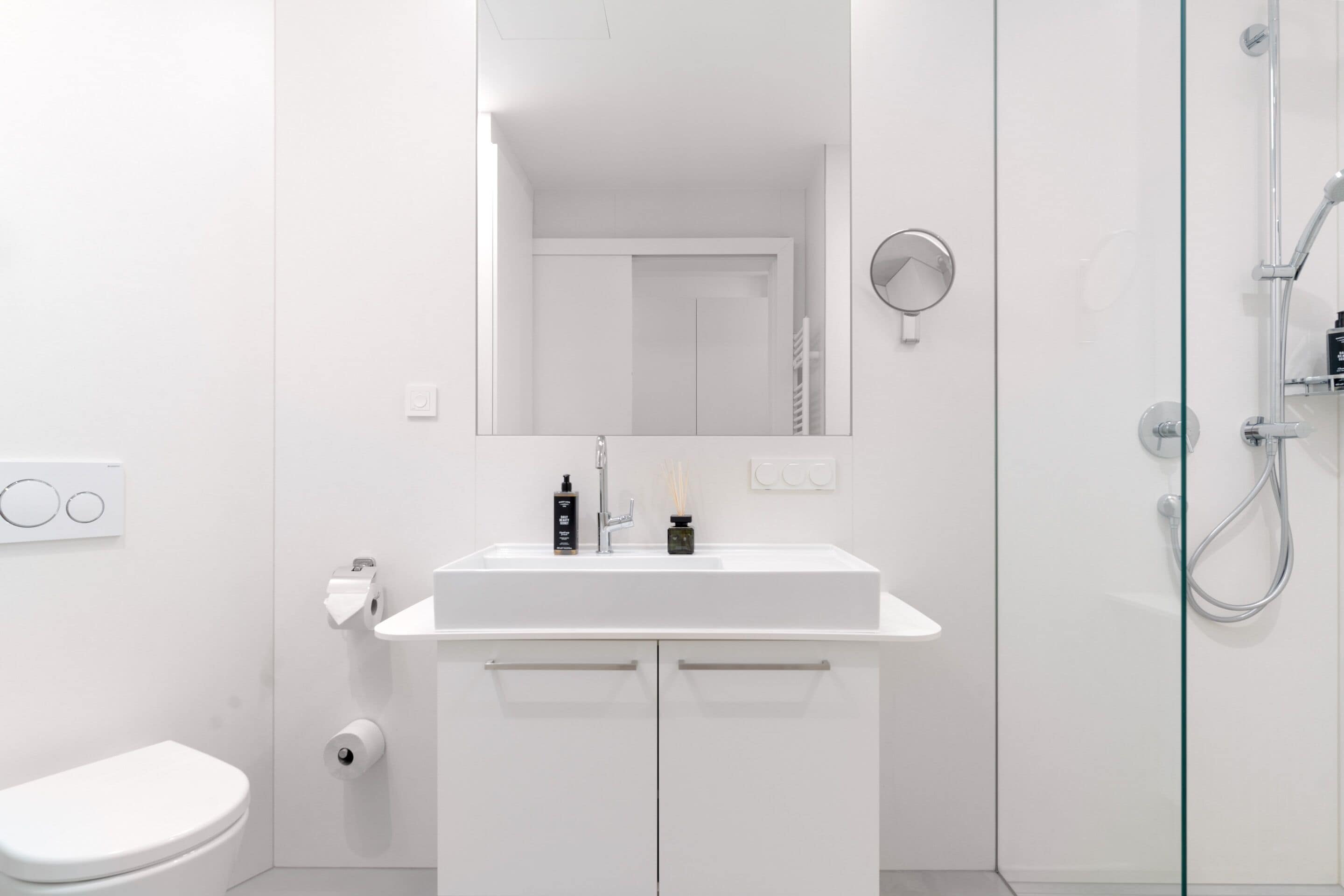 Un bagno moderno con lavandino, specchio, WC e doccia, tutti in bianco.