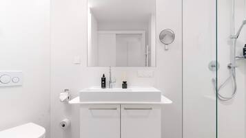Un bagno moderno con lavandino, specchio, WC e doccia, tutti in bianco.