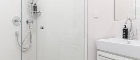 Un baño moderno con cabina de ducha de vidrio, un lavamanos blanco y un espejo encima.