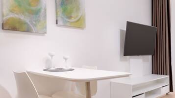 Een moderne hotelkamer met een ronde eettafel, witte stoelen, een flatscreen televisie en abstracte schilderijen aan de muur.