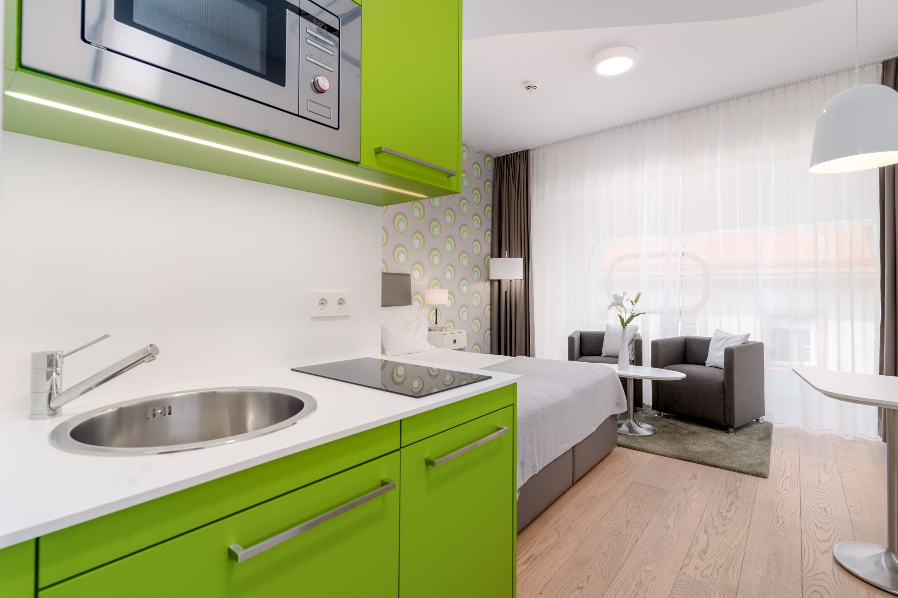 A modern kitchen with a stainless steel sink, green cabinets, and a microwave.