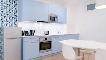 Een moderne keuken met lichtblauwe kastjes, een ingebouwde magnetron, een koffiezetapparaat en een broodrooster. Links staat een witte koelkast en er is een witte eettafel met stoelen.