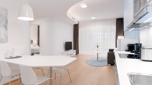 Une chambre d’hôtel moderne dotée d’un coin repas, d’une kitchenette et d’une grande fenêtre avec des rideaux.