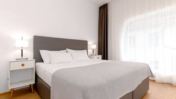 Ein modernes Hotelzimmer mit einem großen Bett, zwei Nachttischen mit Lampen und Blick auf ein Gebäude durch leichte Vorhänge.