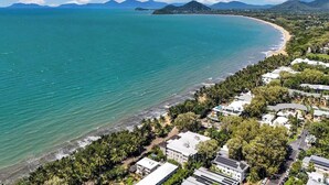 Vue aérienne d’une zone côtière avec une plage, des bâtiments et des montagnes en arrière-plan.