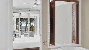 Une salle de bain moderne dotée d’un grand miroir, d’une baignoire et d’une porte coulissante en verre donnant sur un balcon aménagé avec du mobilier d’extérieur.