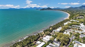 Una zona costiera con spiaggia, edifici residenziali e montagne sullo sfondo.