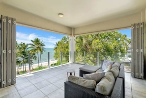 Un balcone con divano e tavolo, vista sulla spiaggia e palme.