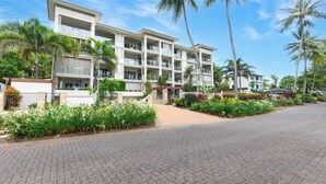 A multi-story hotel with balconies, surrounded by palm trees and landscaped gardens. - Turquesa Tides—Beachfront Resort Living (Palm Cove)