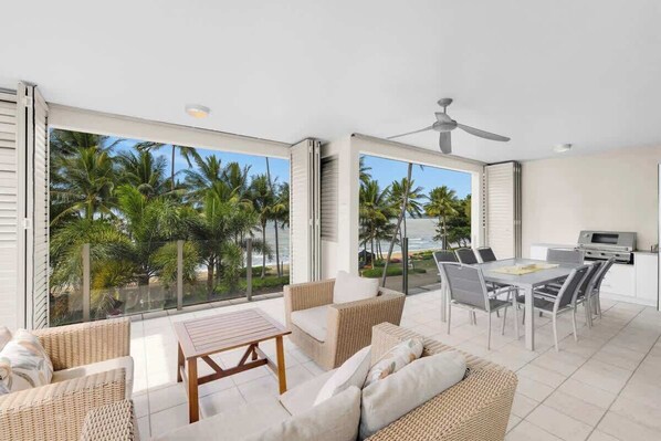 A spacious balcony with a view of palm trees and the ocean, furnished with wicker furniture and a dining area.