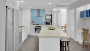 A modern kitchen with white cabinetry, a central island, a blue range hood, and a built-in oven. - Turquesa Tides—Beachfront Resort Living (Palm Cove)