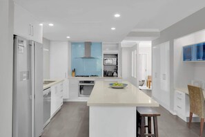 Una cucina moderna con mobili bianchi, un'isola centrale, una cappa aspirante blu e un forno integrato.