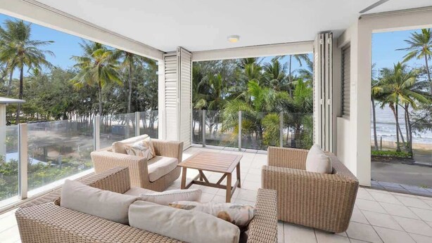 A modern room with a large glass door leading to a balcony with a view of palm trees and a beach. - Turquesa Tides—Beachfront Resort Living (Palm Cove)