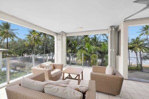 A modern room with a large glass door leading to a balcony with a view of palm trees and a beach. - Turquesa Tides—Beachfront Resort Living (Palm Cove)