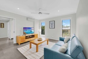 A modern living room with a television, sofa, and a ceiling fan.