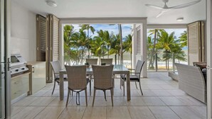 Een moderne keuken met een grill, een eetgedeelte met rieten stoelen, en uitzicht op palmbomen en strand.
