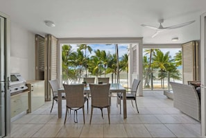 Una cucina moderna con una griglia, zona pranzo con sedie in vimini e vista su palme e spiaggia.